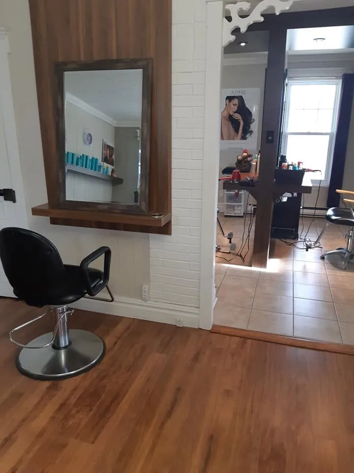 Un fauteuil de coiffure noir devant un miroir à cadre de bois, sur un plancher de bois franc.